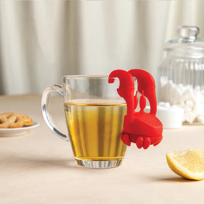 Red tea bag holder in a glass of tea on a table with a lemon and cookies.